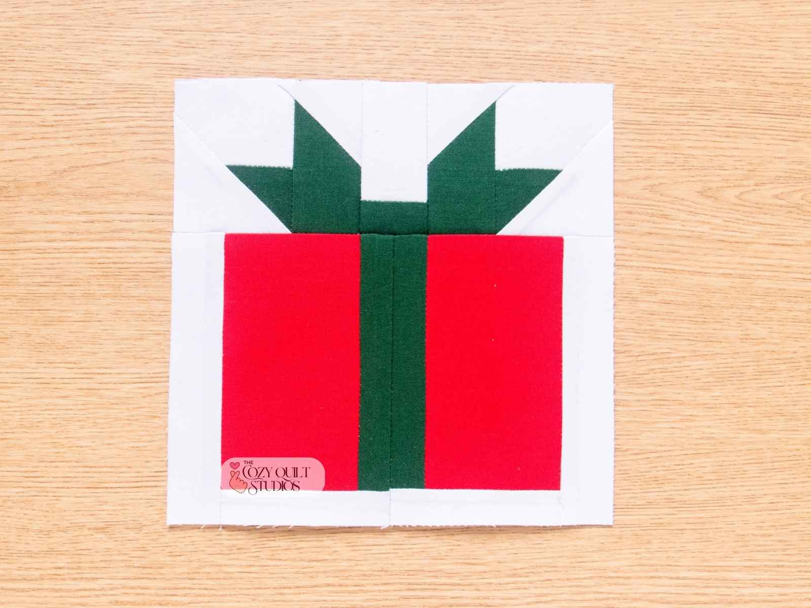 Finished Christmas Present paper pieced quilt block with red and green ribbon bow